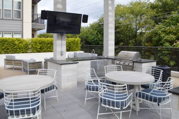 Residences at capitol view outdoor kitchen amenity with patio tables, a outdoor wet bar with built in bbq grill and a tv mounted